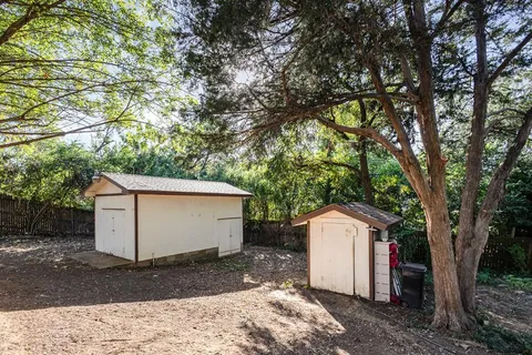 a view of a small white house with a large tree and wooden fence