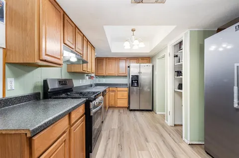 a kitchen with stainless steel appliances granite countertop a refrigerator a sink dishwasher a stove and white countertops with wooden floor