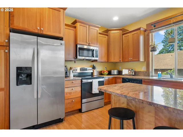 a kitchen with stainless steel appliances granite countertop a refrigerator a stove a sink dishwasher and wooden cabinets with wooden floor