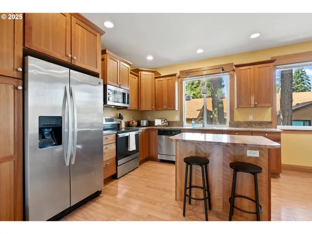 a kitchen with stainless steel appliances granite countertop a refrigerator a sink dishwasher a stove and white countertops with wooden floor