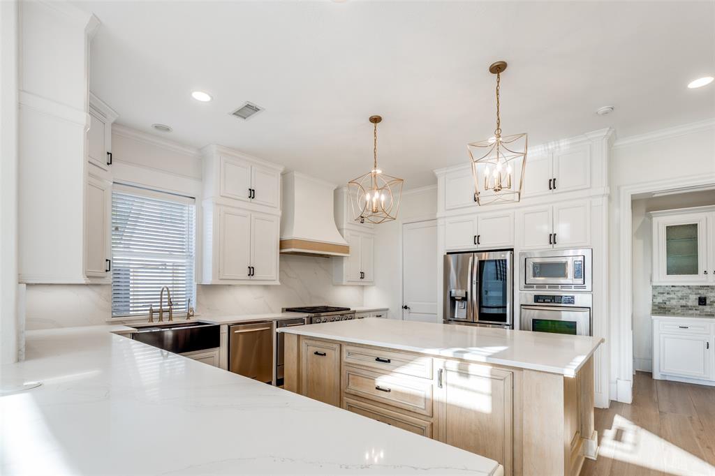 4111 Angling Lane Spring, TX 77386 - Photo 7 of 27 Two tone kitchen featuring stainless steel appliances, tasteful backsplash, a kitchen island, suspended lighting, and light stone countertops
