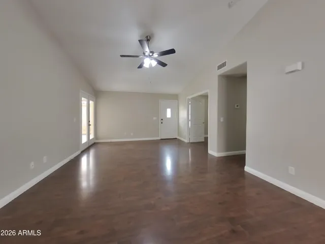 a view of an empty room with wooden floor and a ceiling fan