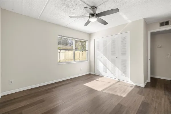 an empty room with wooden floor fan and windows