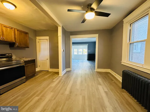 a view of an empty room and kitchen with wooden floor