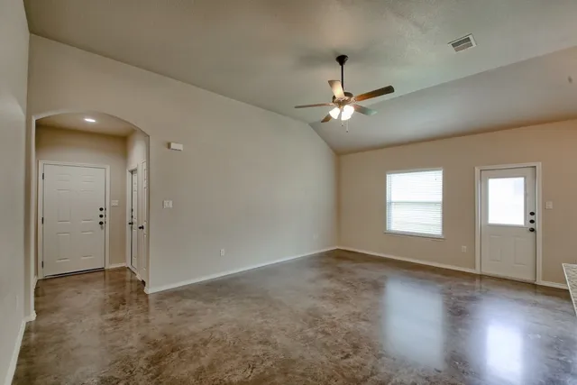 an empty room with chandelier fan and windows