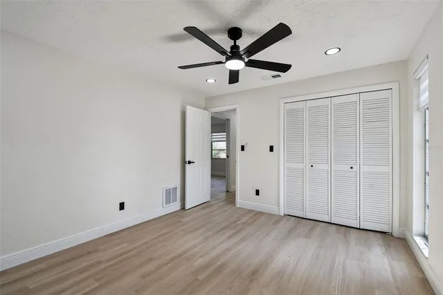 a view of an empty room with wooden floor and a ceiling fan