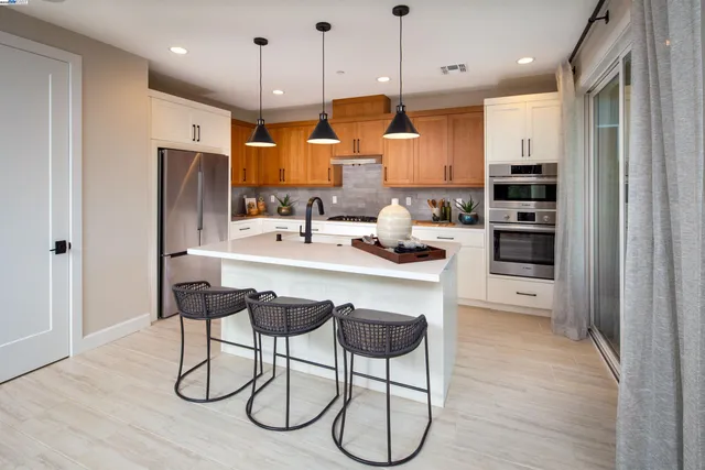 a kitchen with stainless steel appliances kitchen island granite countertop a refrigerator a stove a sink and white cabinets with wooden floor