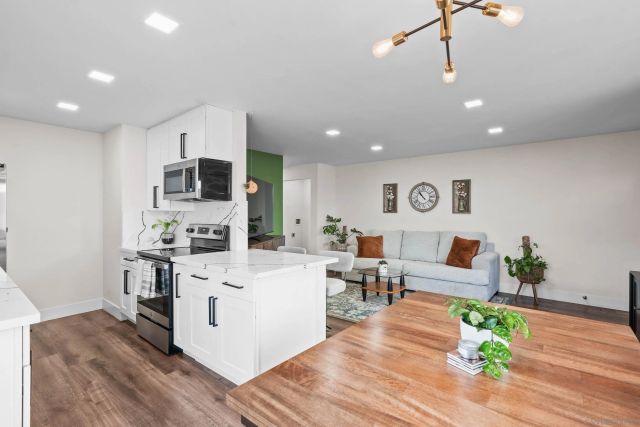 a living room with stainless steel appliances furniture wooden floor and a view of kitchen