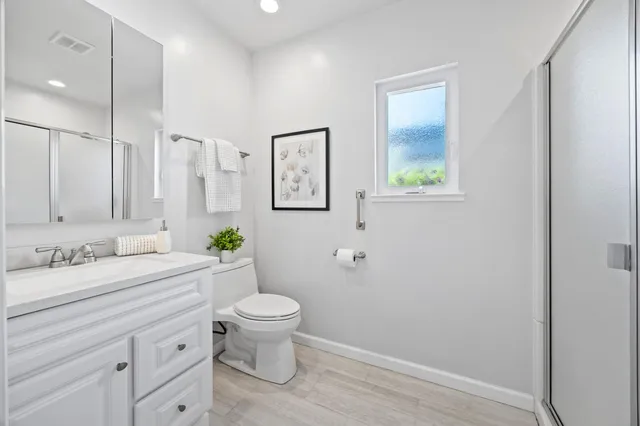 a bathroom with a granite countertop sink toilet a large mirror a shower and a window
