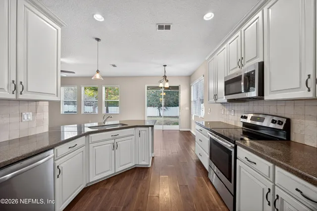 a kitchen with stainless steel appliances a sink dishwasher a stove top oven a refrigerator with wooden floors and cabinets