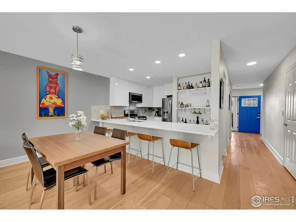 a kitchen with stainless steel appliances kitchen island granite countertop a dining table chairs sink and white cabinets
