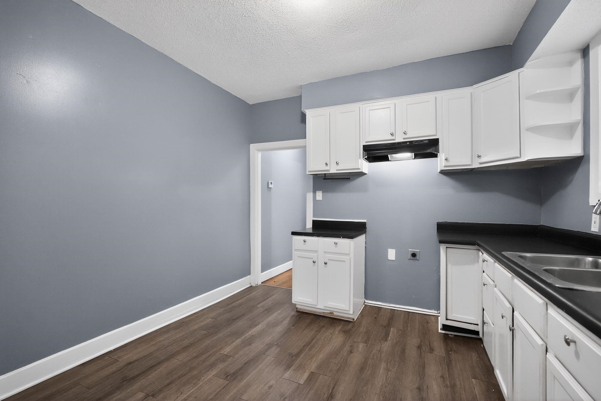 4199 Auburn Road Memphis, TN 38116 - Photo 19 of 32 Kitchen featuring white cabinetry with brushed nickel hardware, dark countertops, a double basin stainless steel sink, and wood-finish flooring