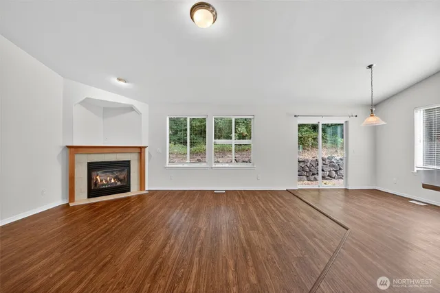 a view of an empty room with wooden floor fireplace and a window