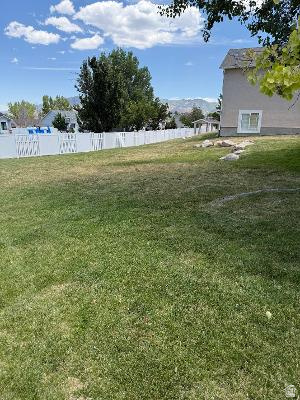 641 East Greystone Way Tooele, UT 84074 - Photo 27 of 30 Spacious backyard featuring a white vinyl privacy fence, mature trees, and a mountain backdrop
