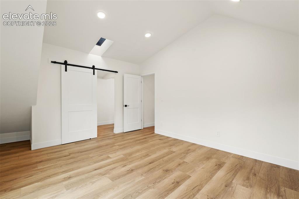 11665 Greentree Road Colorado Springs, CO 80908 - Photo 21 of 43 Unfurnished bedroom featuring a barn door, vaulted ceiling, light wood finished floors, and recessed lighting
