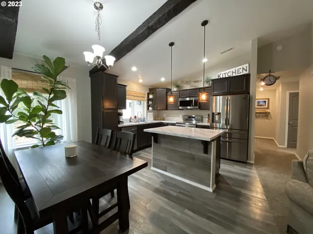 a open kitchen with stainless steel appliances granite countertop a stove a refrigerator a kitchen island a dining table and chairs with wooden floor