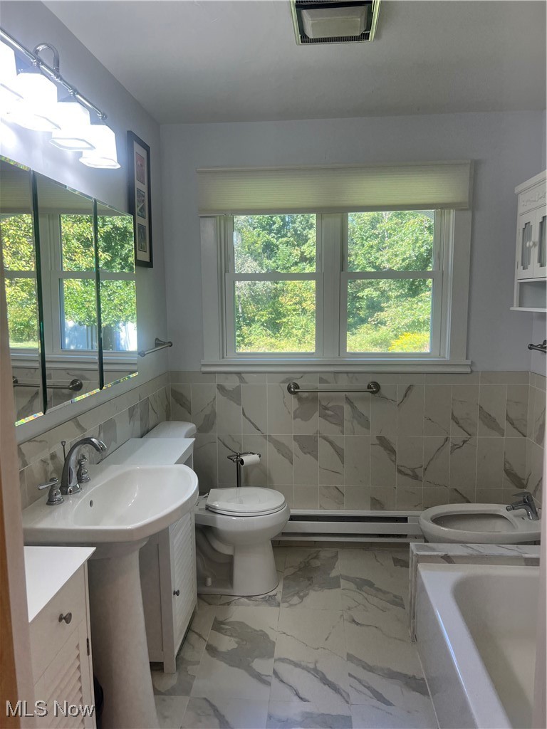 6171 Barrett Road Geneva, OH 44041 - Photo 23 of 38 Full bathroom featuring tile walls, wainscoting, light marble finish floors, baseboard heating, and a bath
