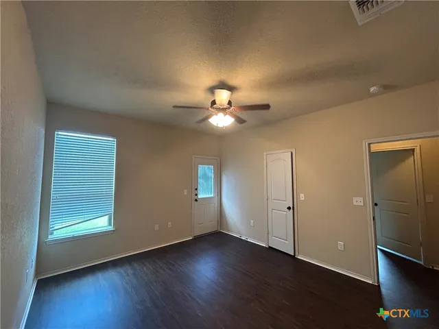an empty room with wooden floor fan and windows