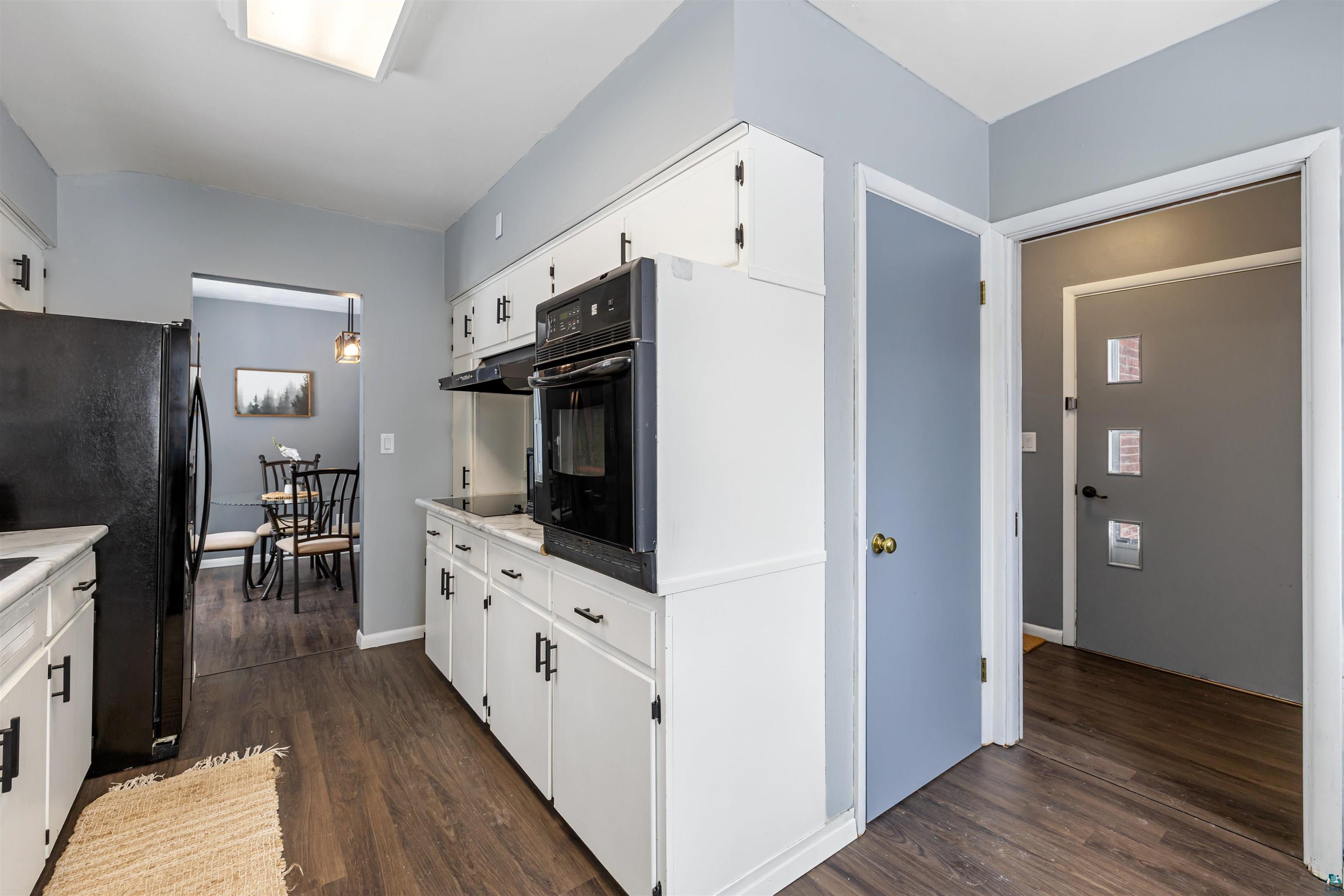 1101 13th Street South Virginia, MN 55792 - Photo 16 of 43 Kitchen featuring dark laminate flooring, white cabinetry, black appliances, cooktop, wall oven, and light laminate countertops