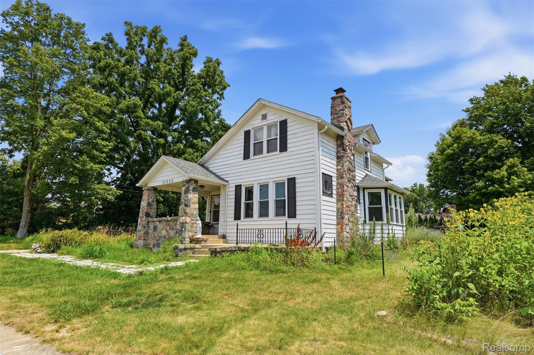 31000 Drake Road Farmington, MI 48331 - Photo 2 of 44 Traditional white siding exterior featuring a stone chimney and a covered front porch with stone pillars