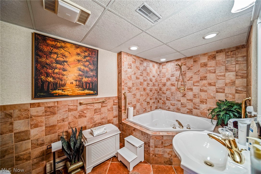 8801 Bunker Road Orwell, OH 44076 - Photo 47 of 50 Bathroom with tile walls, a drop ceiling, tiled shower / bath, a baseboard radiator, and tile patterned floors