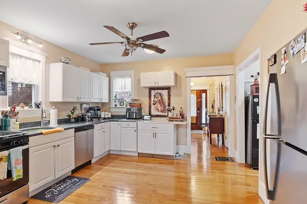 a kitchen with stainless steel appliances granite countertop a refrigerator a sink dishwasher a stove with white cabinets and wooden floor