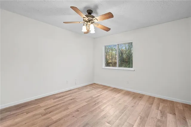 an empty room with wooden floor ceiling fan and window