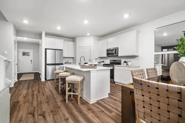 a kitchen with stainless steel appliances kitchen island granite countertop a refrigerator a stove a sink a dining table and chairs with wooden floor
