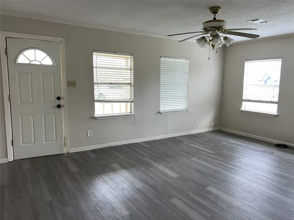 an empty room with wooden floor chandelier fan and windows