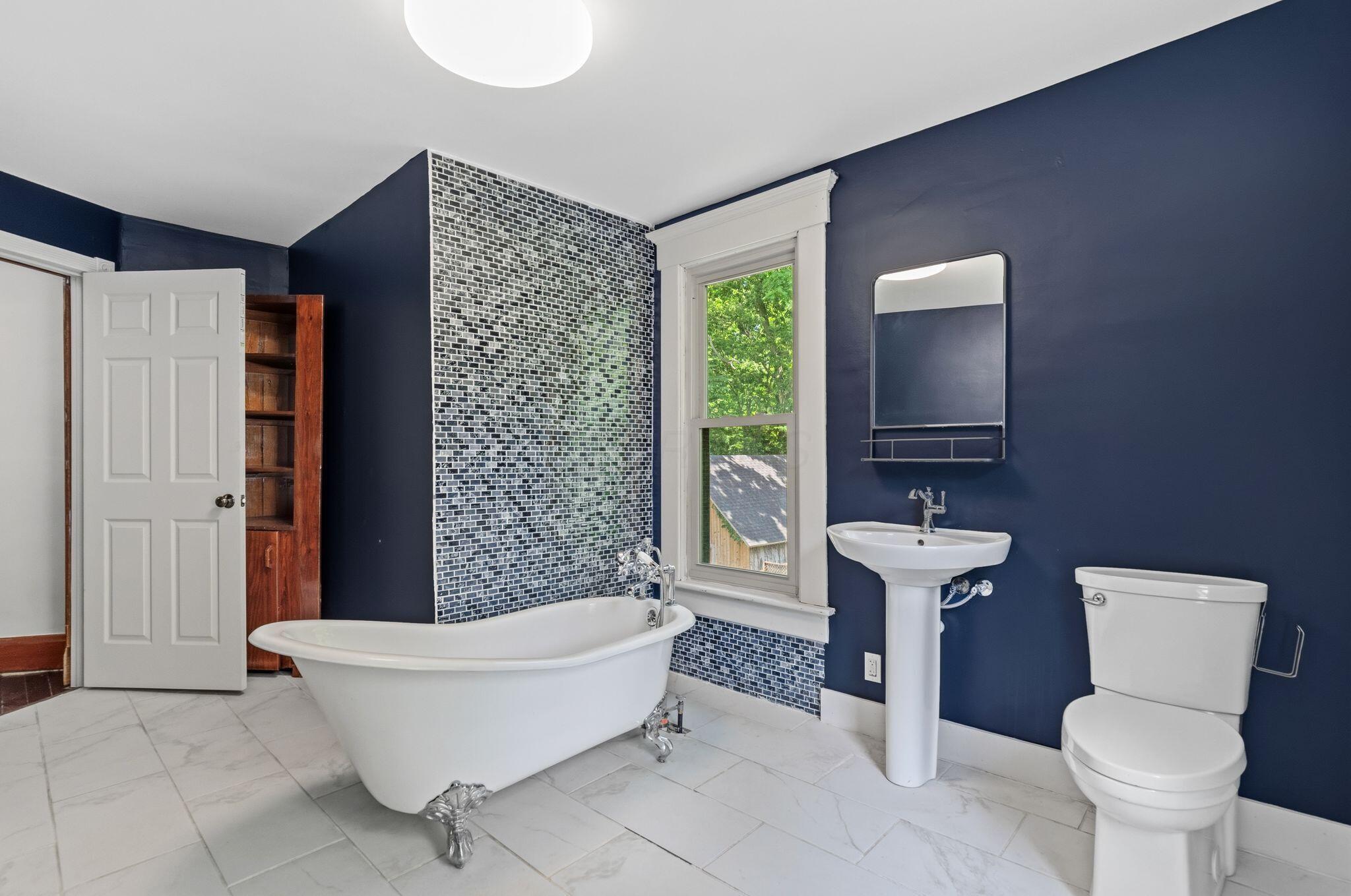 107 Price Road Columbus, OH 43230 - Photo 25 of 51 Bathroom featuring a clawfoot tub, pedestal sink, and mosaic tile accent wall
