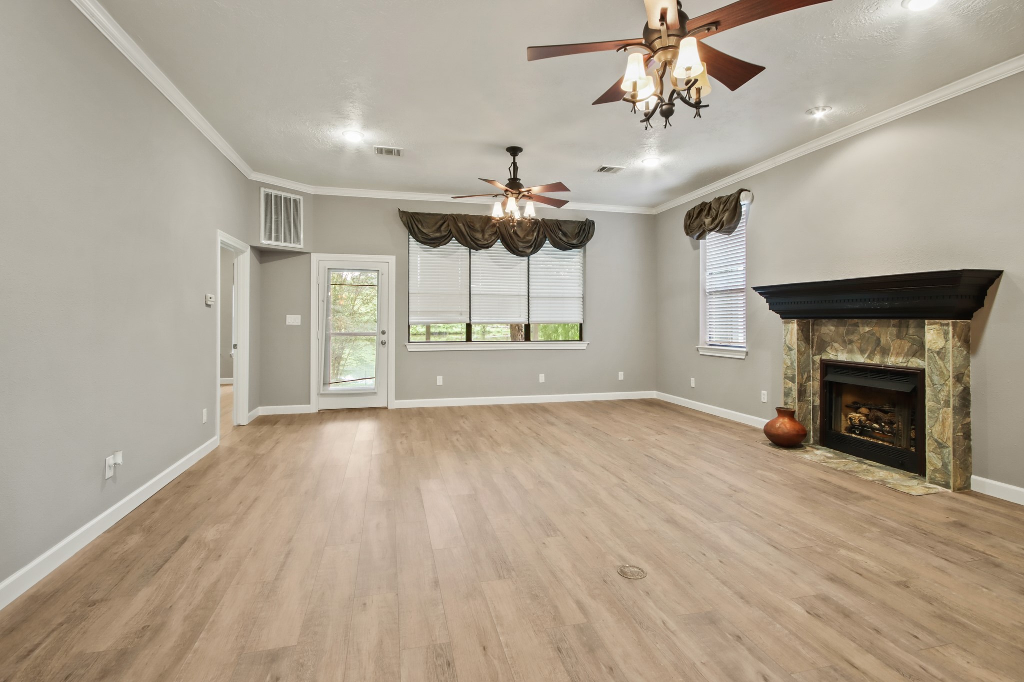 35 Susan Drive Cleveland, TX 77327 - Photo 5 of 33 Bright and spacious living room with light wood flooring, a stone fireplace, and large windows. Features a ceiling fan with lights and access to a patio through a glass door.