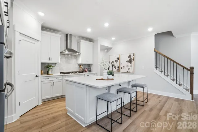 a kitchen with stainless steel appliances a sink dishwasher a stove a refrigerator and white cabinets with wooden floor