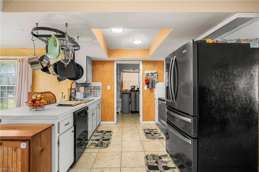 115 Georgia Road Lehigh Acres, FL 33936 - Photo 10 of 26 Kitchen with black appliances, a sink, light countertops, a tray ceiling, and light tile patterned flooring