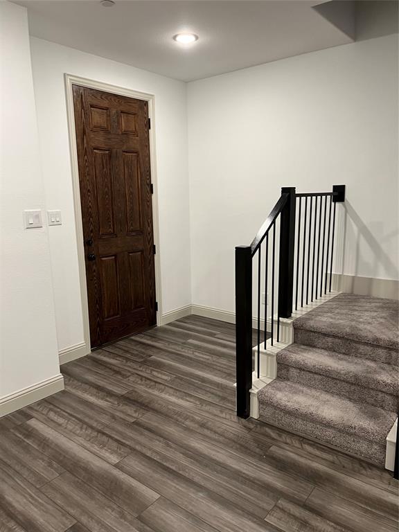 6041 Roper Road McKinney, TX 75070 - Photo 5 of 24 Entryway featuring wood-finish flooring, a dark wood paneled door, recessed ceiling lighting, and a carpeted staircase with a black metal railing