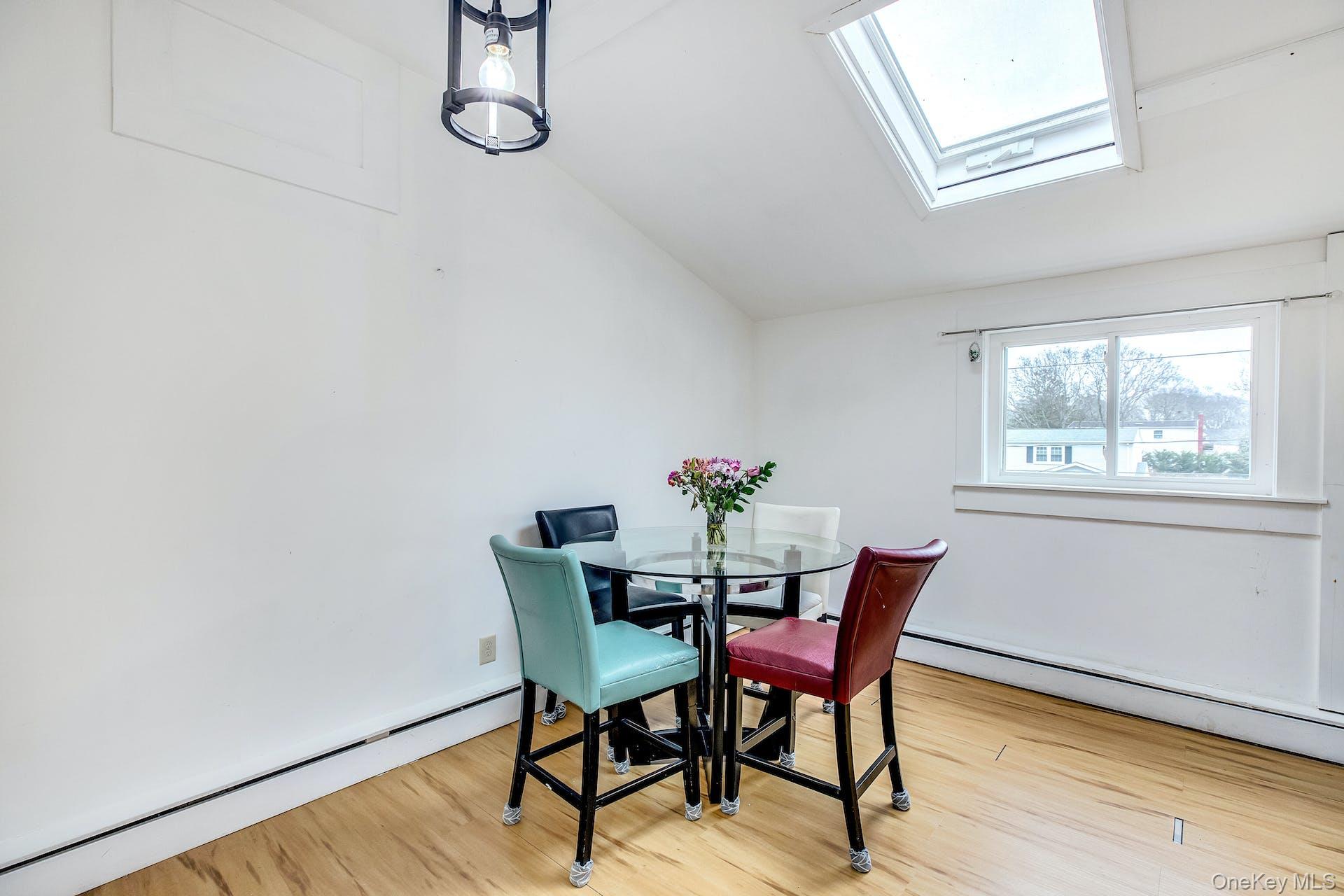7 George Street Hampton Bays, NY 11946 - Photo 11 of 11 Room featuring wood-finish flooring, a prominent skylight, a large window, a vaulted ceiling, and a modern ceiling light fixture
