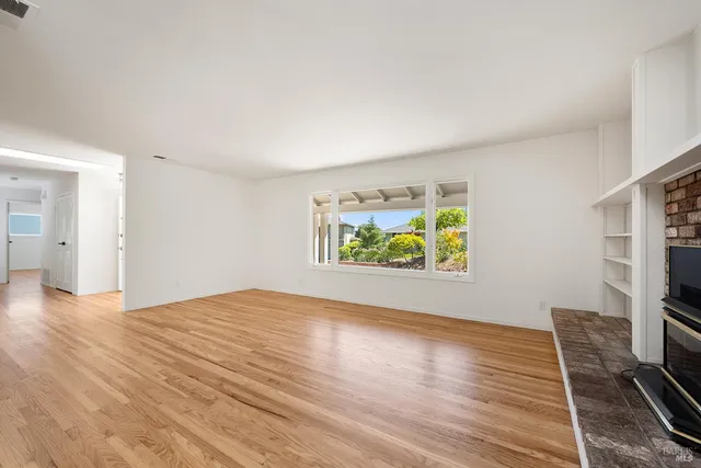 a view of an empty room with window a ceiling fan and wooden floor