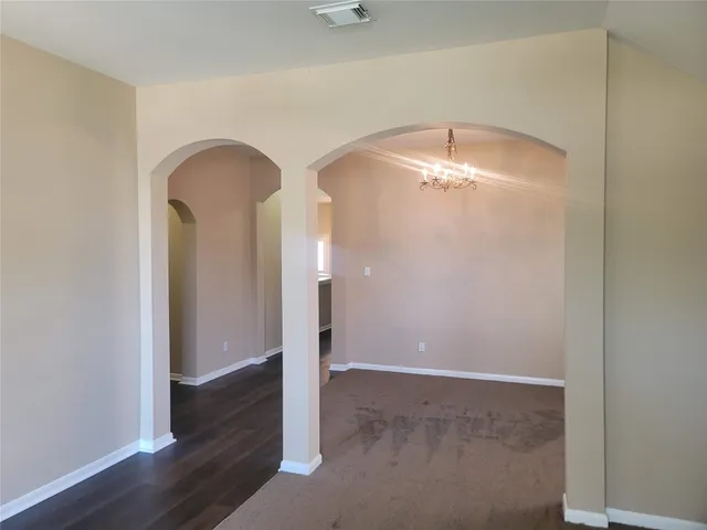 an empty room with wooden floor and way to kitchen