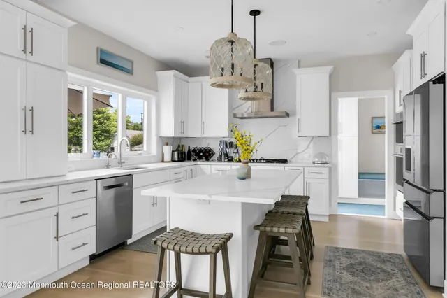 a kitchen with stainless steel appliances kitchen island granite countertop a refrigerator a sink dishwasher a stove a dining table and chairs with wooden floor