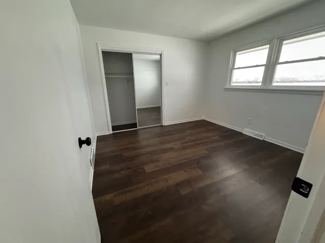 an empty room with wooden floor cabinet and windows