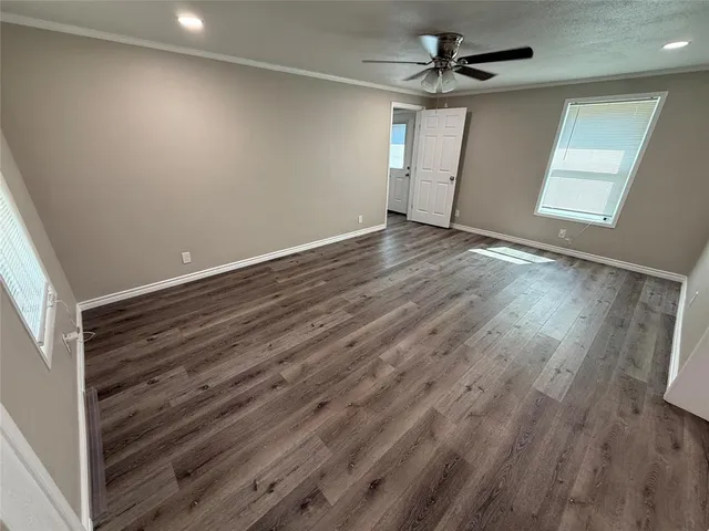 an empty room with wooden floor ceiling fan and windows