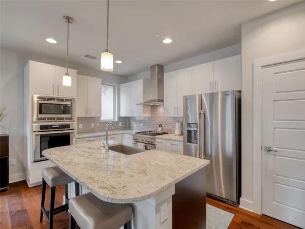 a kitchen with stainless steel appliances granite countertop a stove a sink a refrigerator and white cabinets