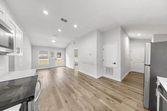a view of an empty room with wooden floor and a kitchen