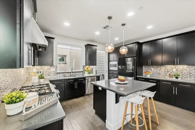 a kitchen with stainless steel appliances kitchen island granite countertop a stove a sink dishwasher and a refrigerator with wooden floor