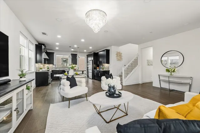a living room with lots of furniture kitchen view and a chandelier