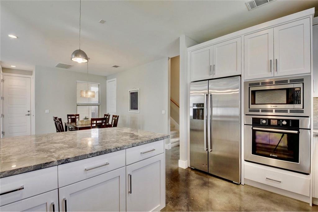 701 East 49th Street, Unit B Austin, TX 78751 - Photo 5 of 27 Kitchen with white cabinetry, built in appliances, finished concrete floors, light stone countertops, and pendant lighting