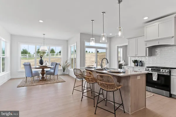 a kitchen with stainless steel appliances granite countertop a stove a refrigerator a sink a dining table and chairs with wooden floor