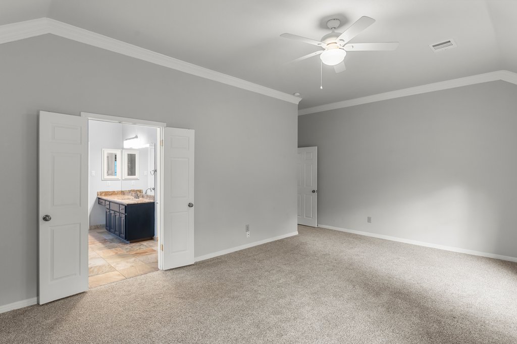 1406 Dapplegrey Lane Austin, TX 78727 - Photo 15 of 38 Unfurnished bedroom featuring light colored carpet, ornamental molding, lofted ceiling, connected bathroom, and a ceiling fan