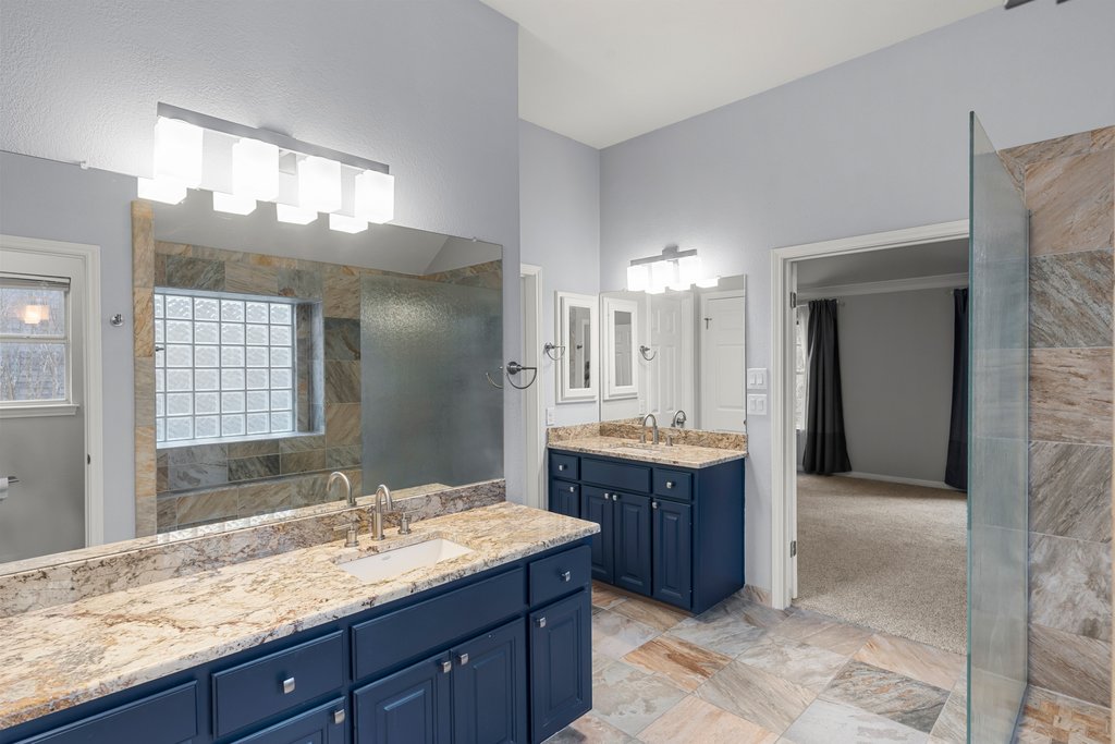 1406 Dapplegrey Lane Austin, TX 78727 - Photo 17 of 38 Full bathroom with two vanities, walk in shower, and light stone finish floors