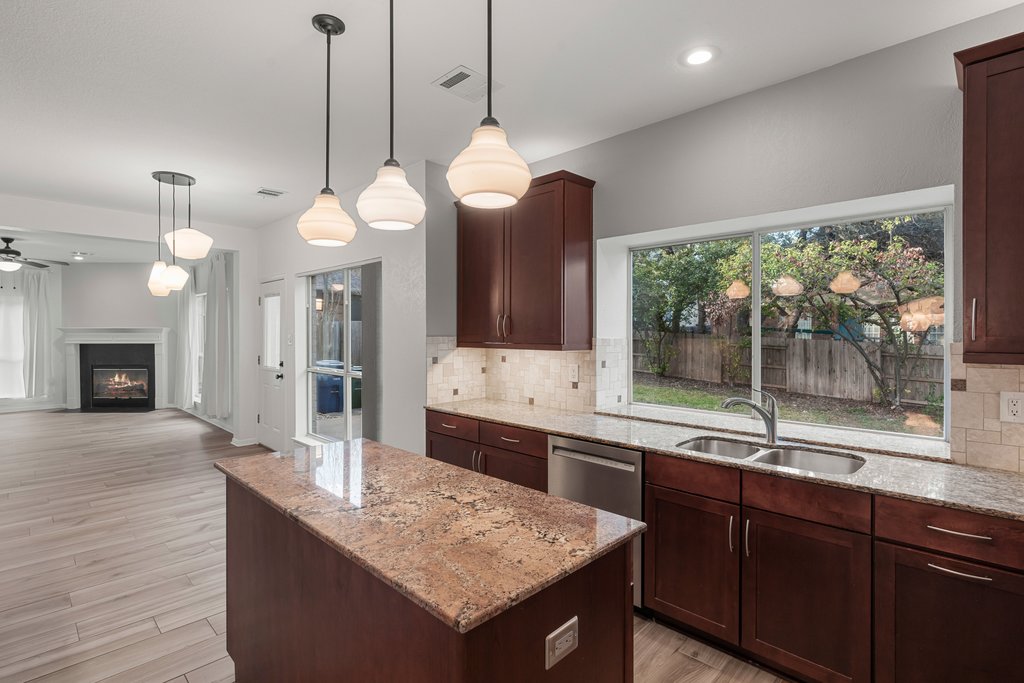 1406 Dapplegrey Lane Austin, TX 78727 - Photo 38 of 38 Kitchen with dark wood finish cabinets, a center island, light stone counters, light wood-type flooring, and open floor plan