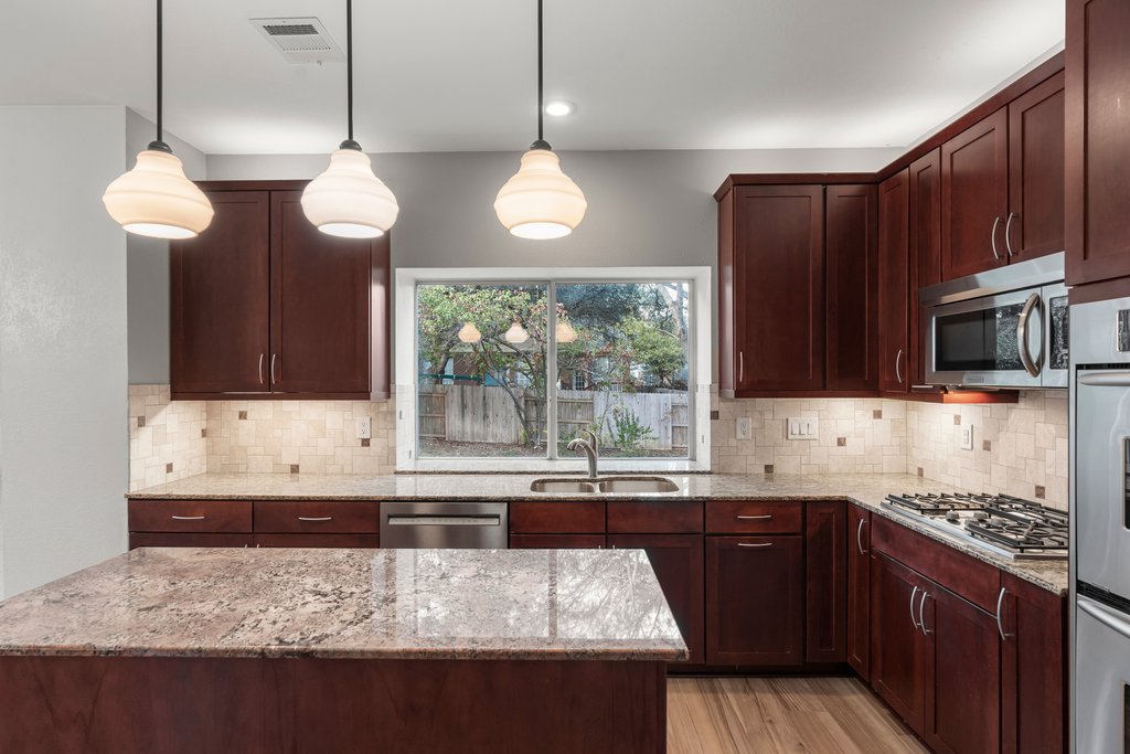 1406 Dapplegrey Lane Austin, TX 78727 - Photo 7 of 38 Kitchen with light stone counters, light wood-style floors, stainless steel appliances, pendant lighting, and decorative backsplash